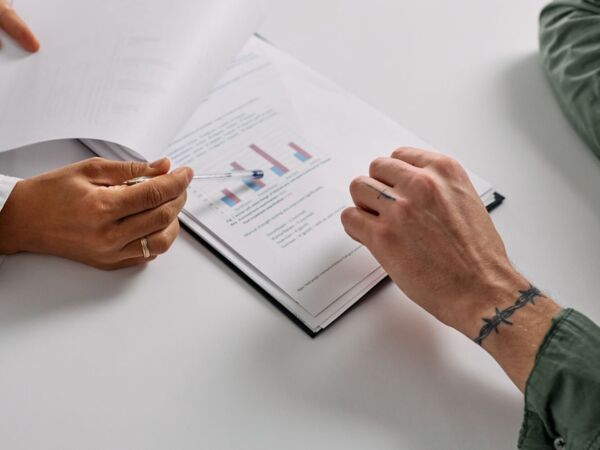Nahaufnahme von Händen, die Dokumente mit Diagrammen überprüfen und Teamarbeit sowie Analyse betonen.