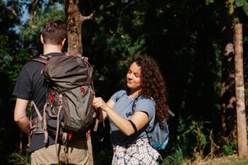 Ein junges Paar auf einem Wanderabenteuer in einem sonnenbeschienenen Wald, Rucksäcke bindend.