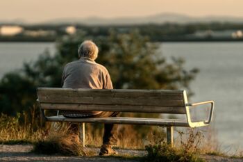 Ruhige Szene eines älteren Mannes, der während des Sonnenuntergangs auf einer Bank am See sitzt.