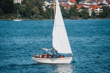 Ein Segelboot gleitet durch ruhige Gewässer mit einer charmanten Stadt am Ufer des Sees im Hintergrund.