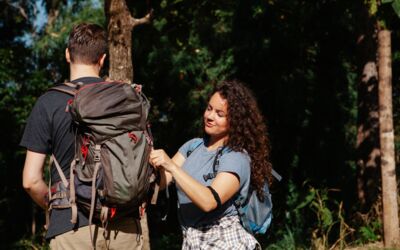 Ein junges Paar auf einem Wanderabenteuer in einem sonnenbeschienenen Wald, Rucksäcke bindend.