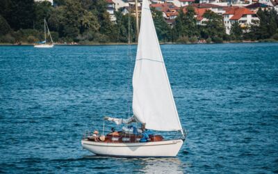 Ein Segelboot gleitet durch ruhige Gewässer mit einer charmanten Stadt am Ufer des Sees im Hintergrund.