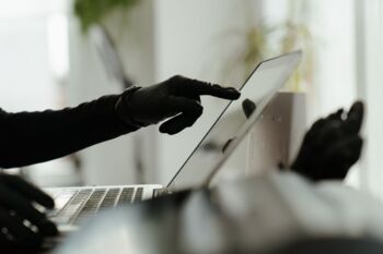 Nahaufnahme einer behandschuhten Hand, die mit einem Laptop in einer eleganten, modernen Büroumgebung interagiert.