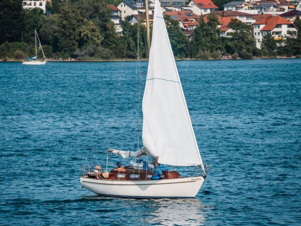 Ein Segelboot gleitet durch ruhige Gewässer mit einer charmanten Stadt am Ufer des Sees im Hintergrund.
