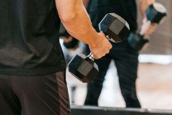 Ein Mann, der mit schweren Kurzhanteln vor einem Spiegel trainiert und Fitness sowie Stärke zeigt.