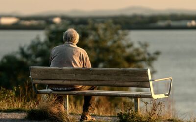 Ruhige Szene eines älteren Mannes, der während des Sonnenuntergangs auf einer Bank am See sitzt.