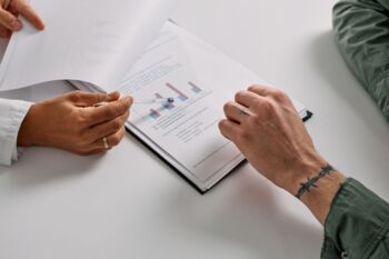 Nahaufnahme von Händen, die Dokumente mit Diagrammen überprüfen und Teamarbeit sowie Analyse betonen.