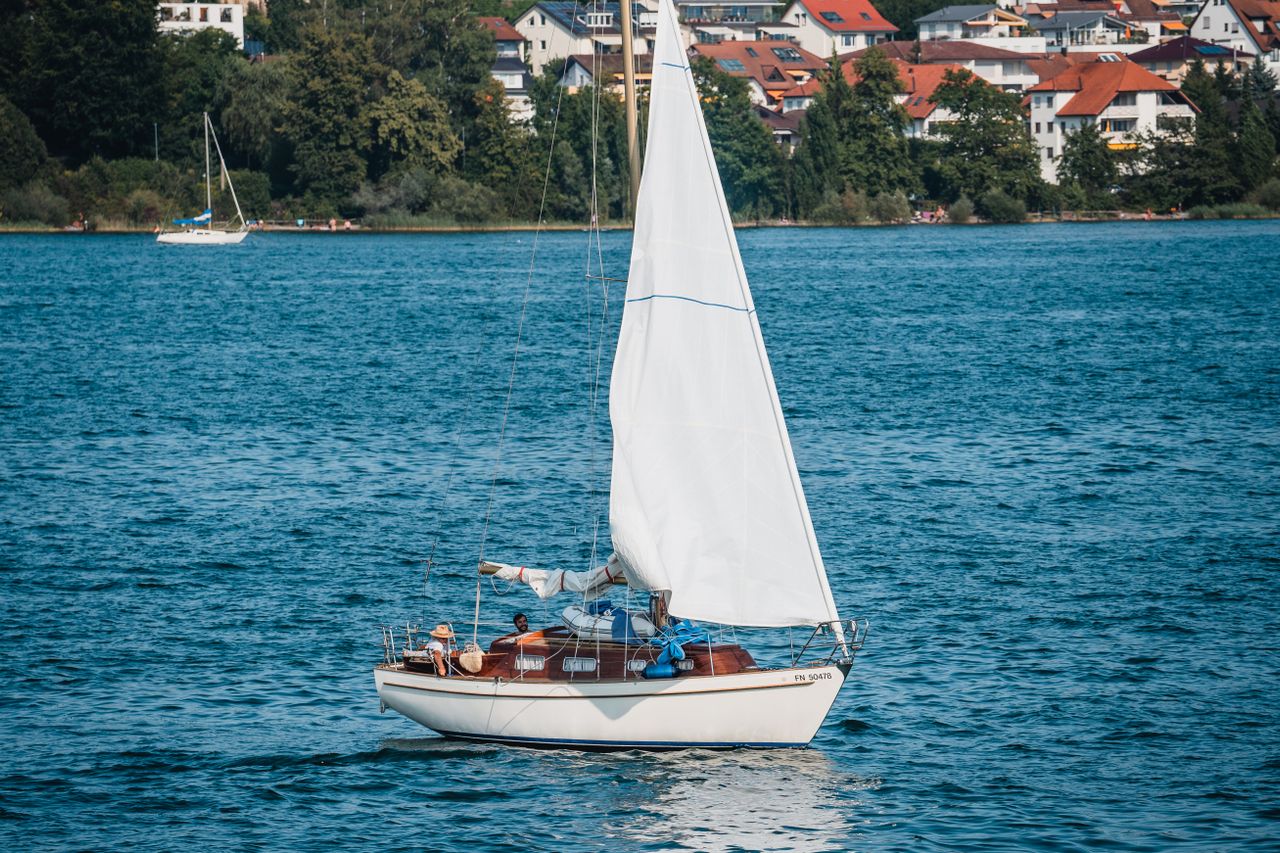 Ein Segelboot gleitet durch ruhige Gewässer mit einer charmanten Stadt am Ufer des Sees im Hintergrund.